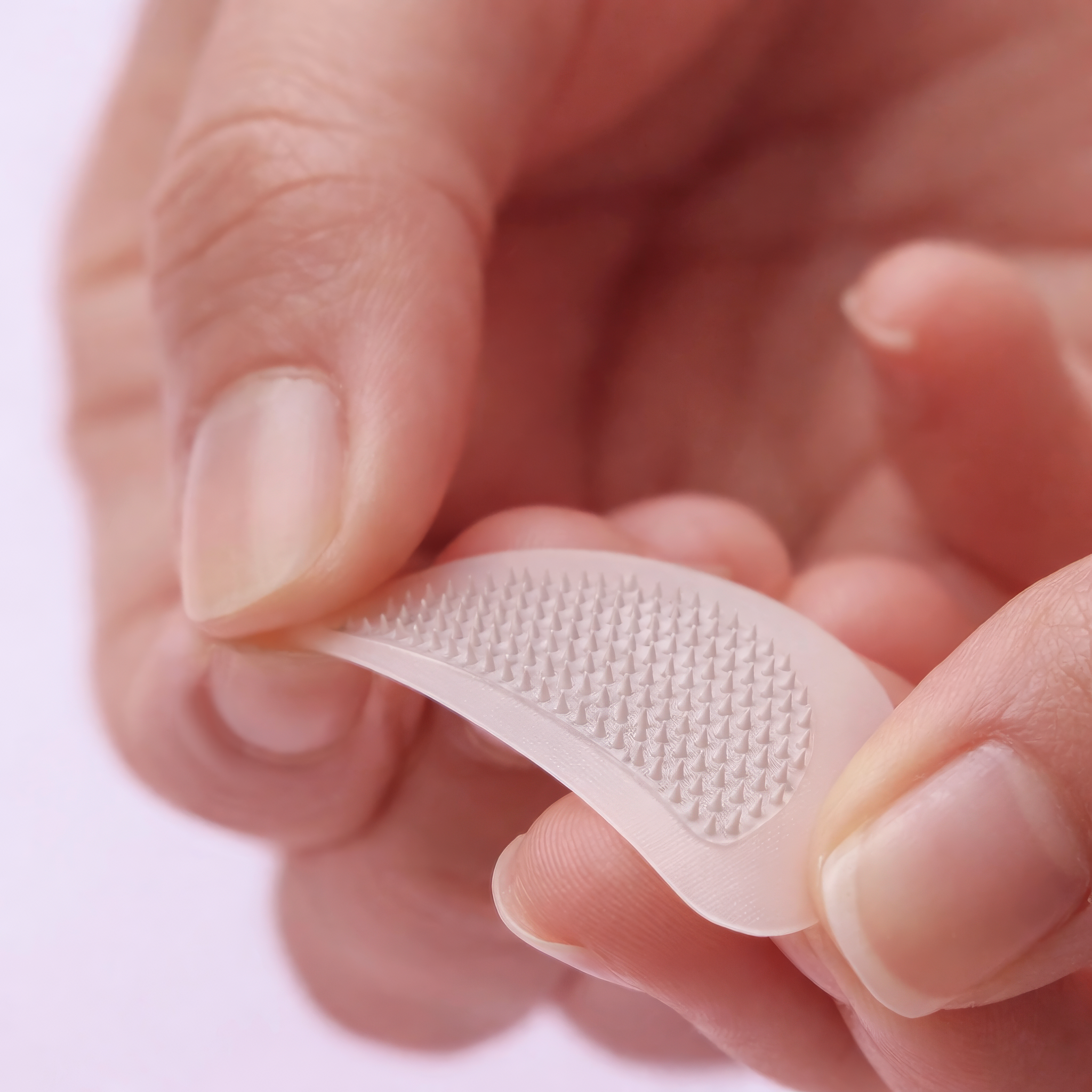 Close-up of a curved CELLUL EYES patch held between fingers, showing the raised array on its surface